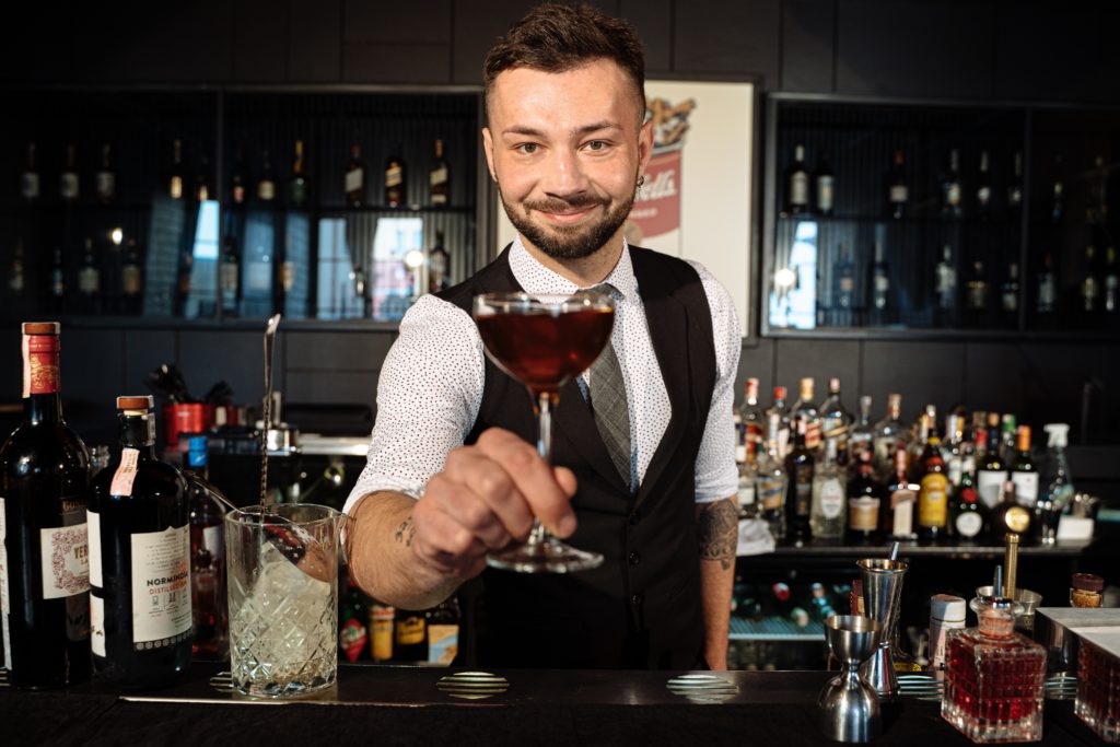 The bartender serves your drink. You say gracias. He says you're welcome in Spanish.